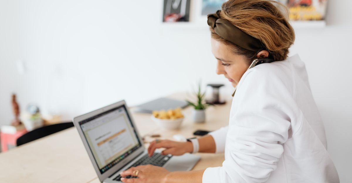 A woman wearing a headset works on a laptop at home while looking into smith ai jobs.
